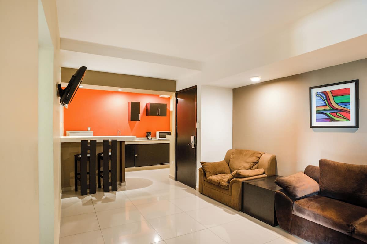 Sala moderna com sofá marrom, mesa de centro e área de cozinha com parede em laranja.