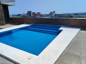 Una piscina rectangular con agua cristalina azul, rodeada por un patio de baldosas.