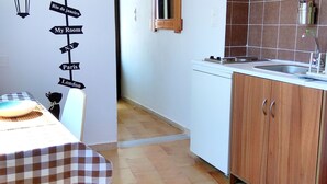 Une cuisine avec un mur recouvert de carreaux, un évier et un meuble en bois. On y trouve une table recouverte d’une nappe à carreaux et un saladier. Un panneau mural indiquant des noms de villes est visible.