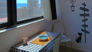 Une pièce avec une table dressée pour deux personnes, une vue sur les bâtiments à l’extérieur et un mur orné d’une illustration de chat et d’indications.