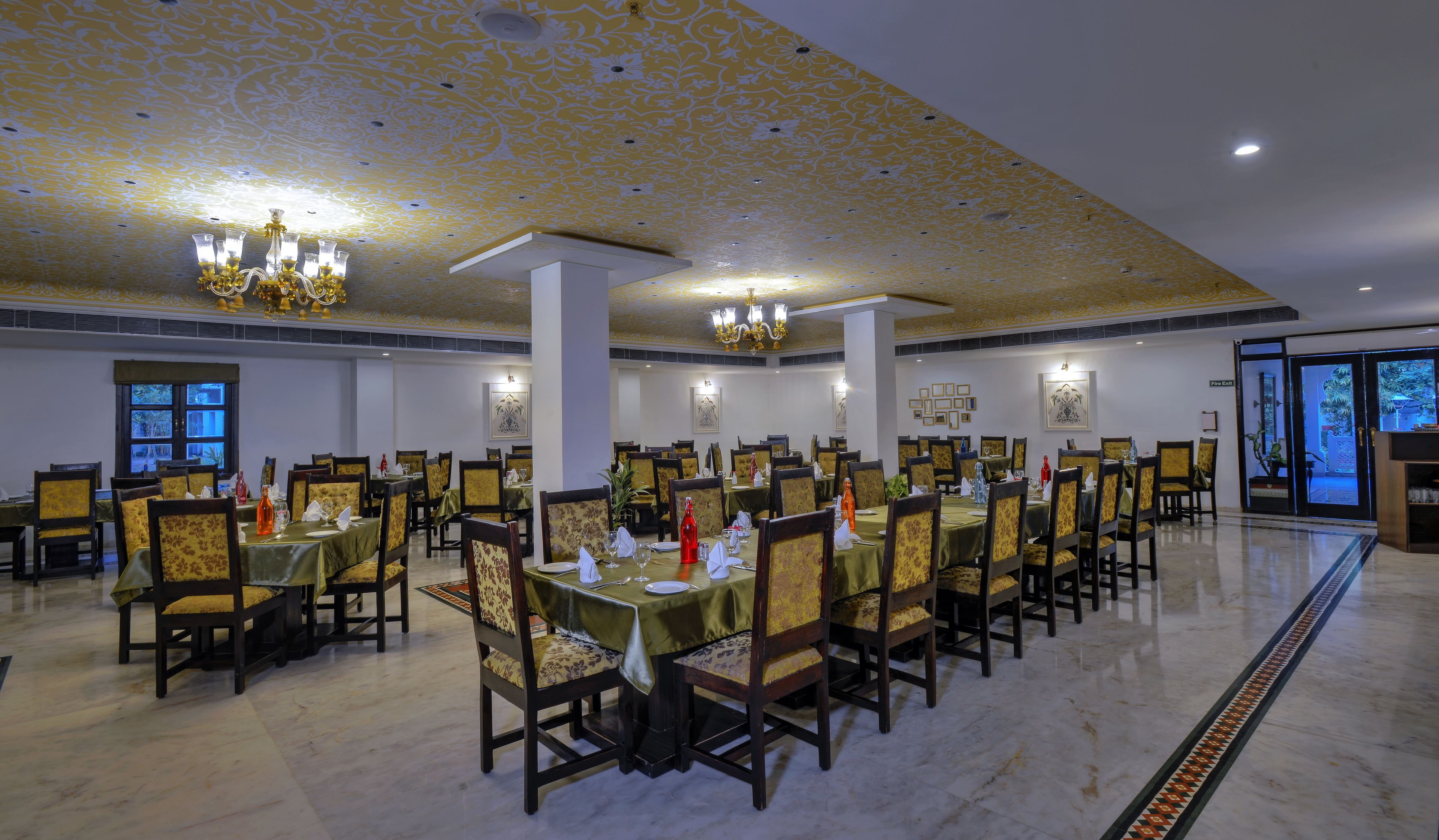 Une grande salle à manger avec de nombreuses tables et chaises, des lustres et des œuvres d’art encadrées accrochées aux murs.