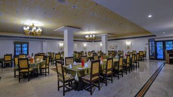 Un amplio comedor con numerosas mesas y sillas, candelabros y cuadros en las paredes.