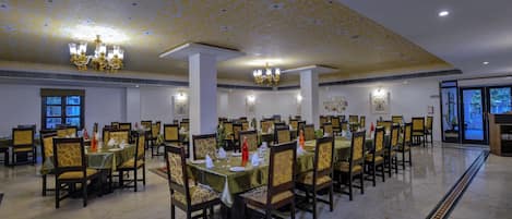 Une grande salle à manger avec de nombreuses tables et chaises, des lustres et des œuvres d’art encadrées accrochées aux murs.