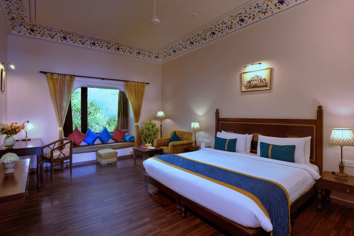 A hotel room with a large bed, a desk with a chair, a TV, and a window with curtains.