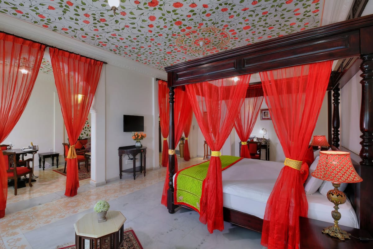 A four-poster bed with red curtains, a television on the wall, and a dining area with a table and chairs.