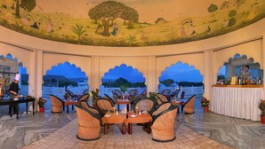 Un restaurante con un mural de paisaje rural, sillas de mimbre, un cocinero preparando comida y una zona de bar.