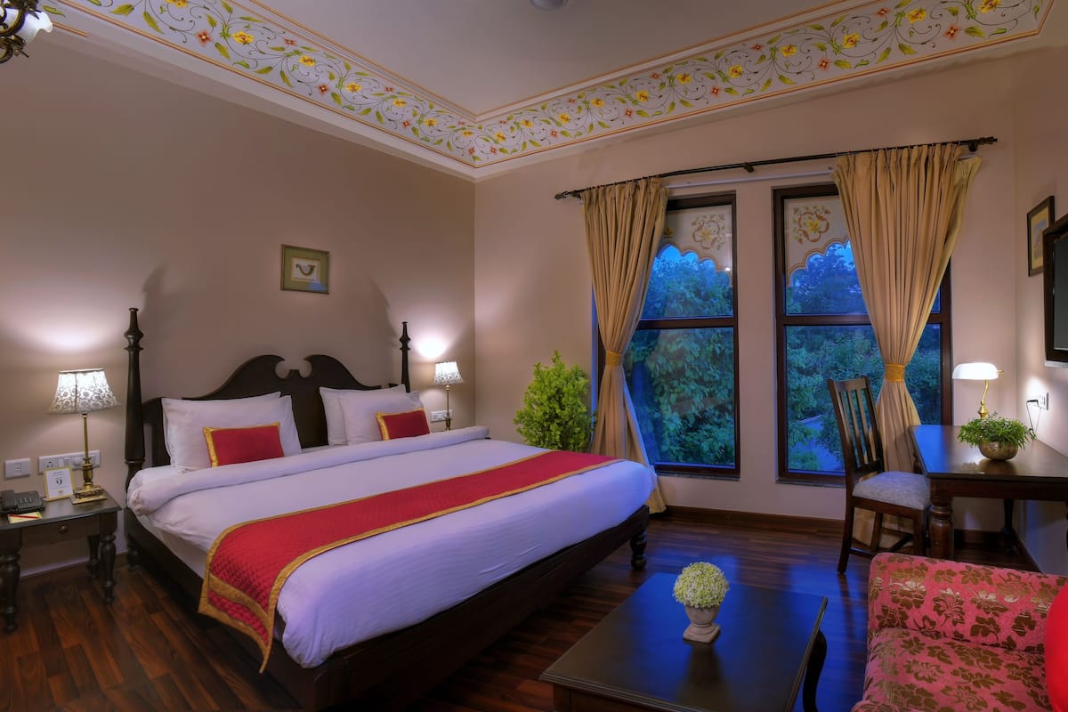 A hotel room with a large bed, a desk with a chair, a TV, and a window with curtains.