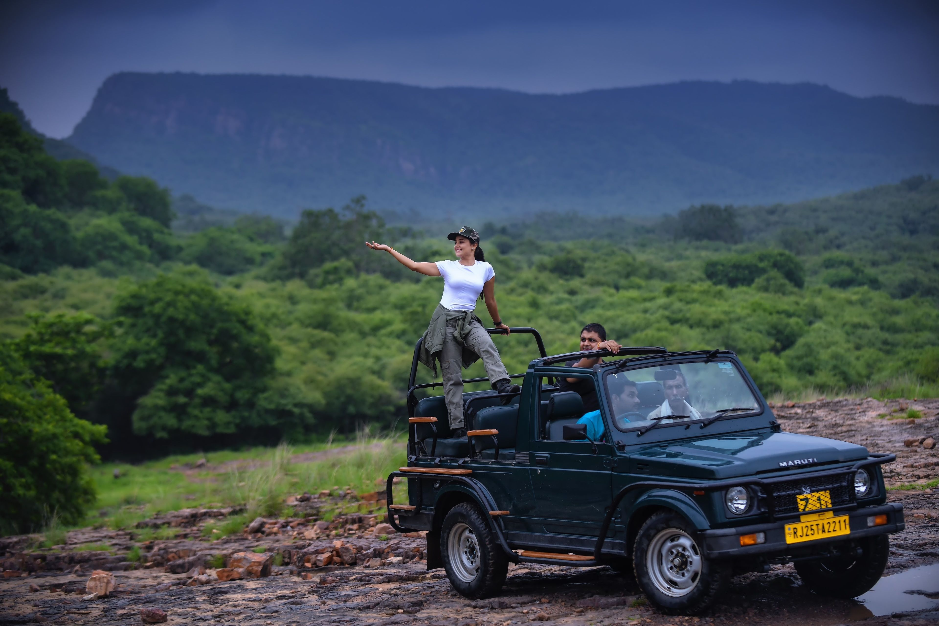 A vehicle parked on a rocky terrain with lush greenery and mountains in the background.