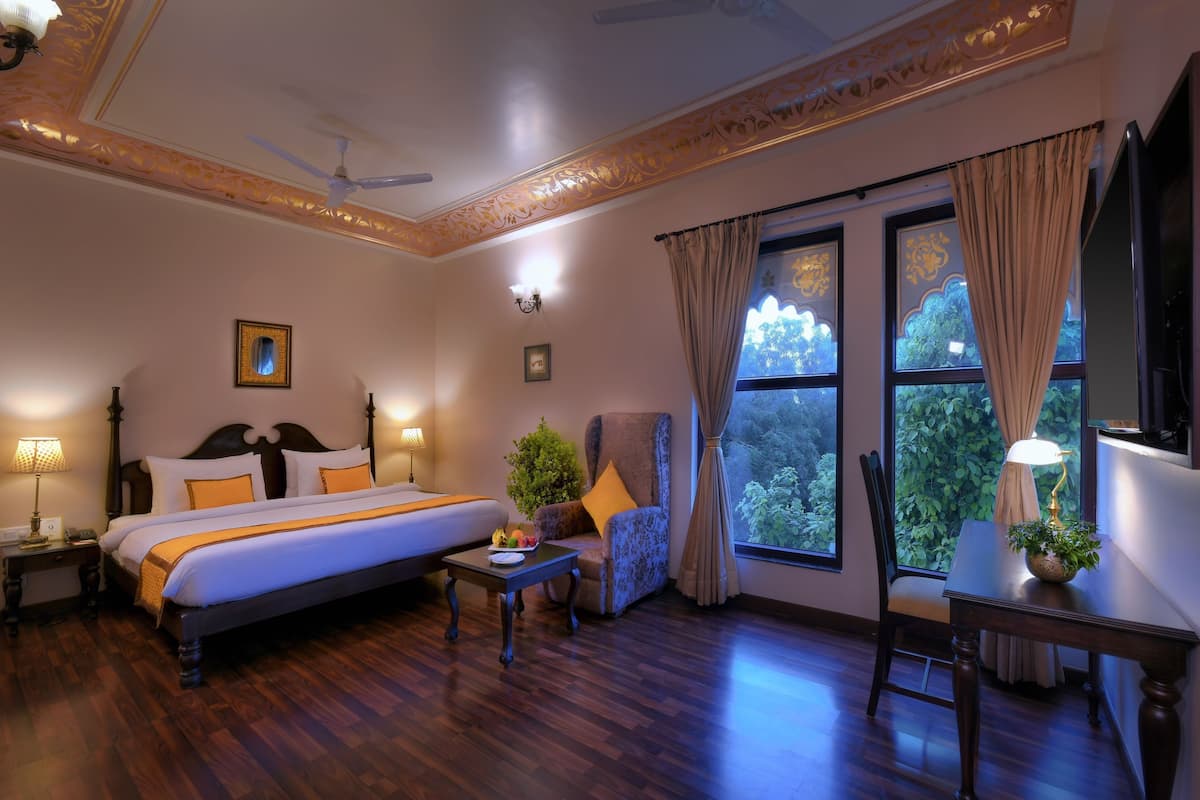 A hotel room with a bed, a chair, a table, a ceiling fan, and a large window with curtains.