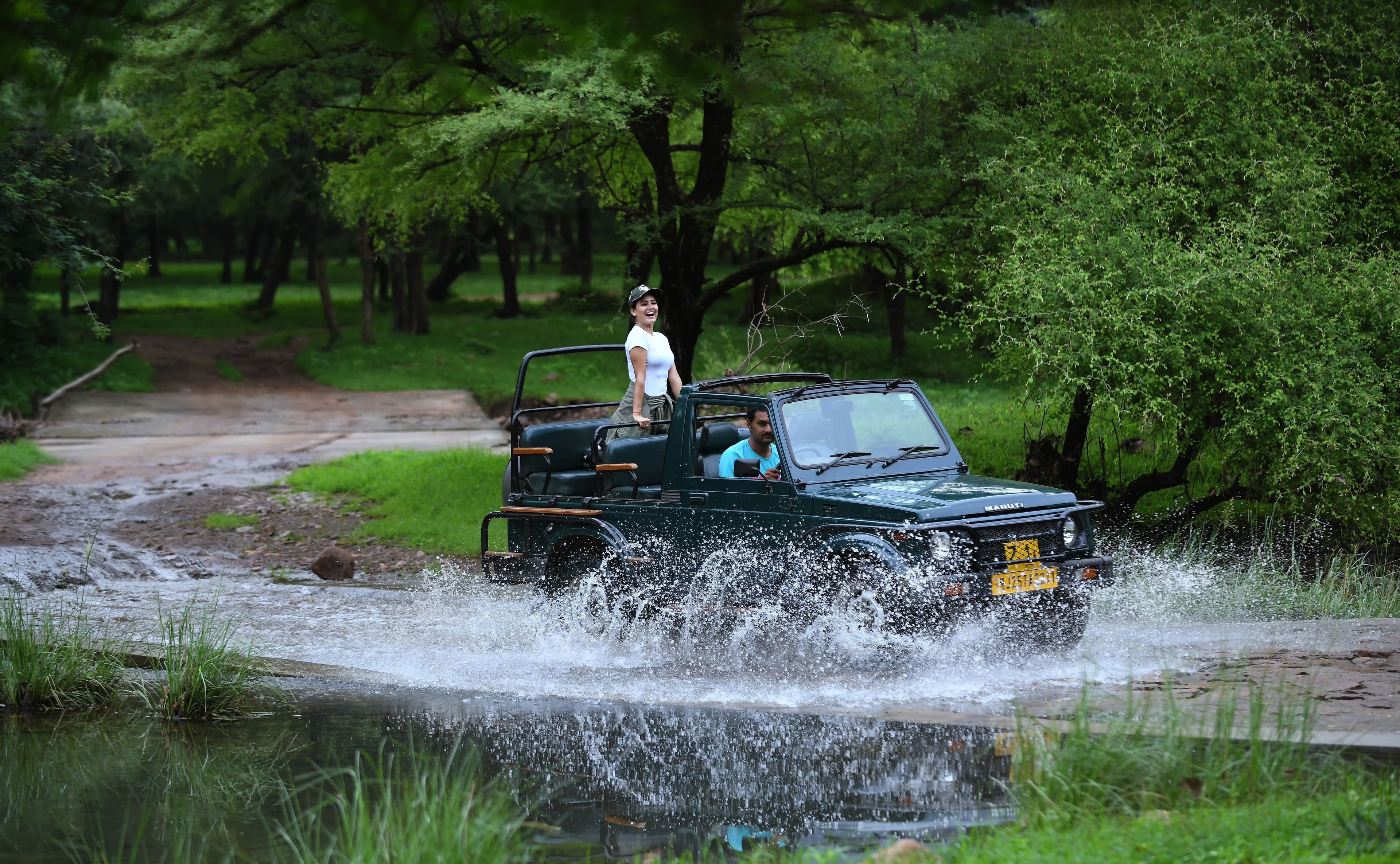 A vehicle driving through a shallow water crossing in a wooded area.