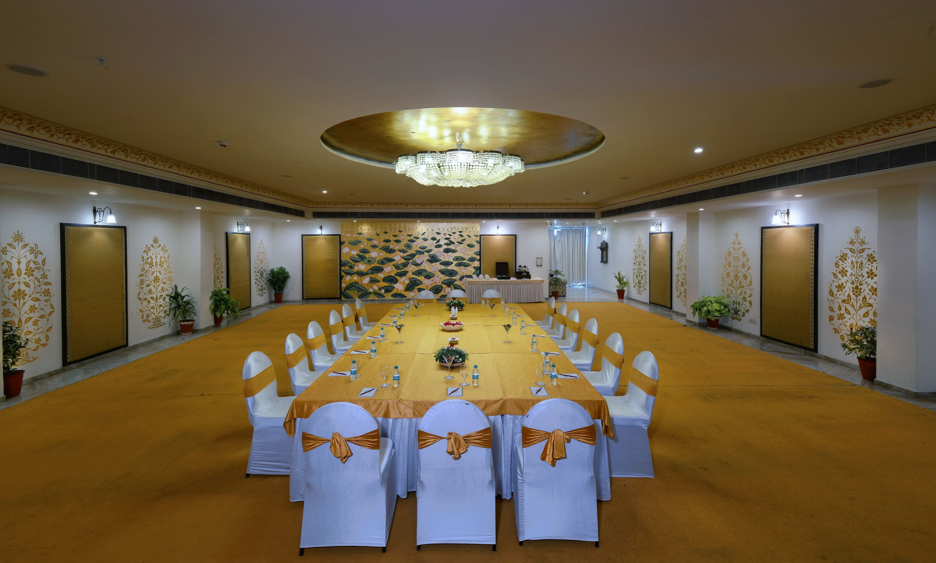 A conference room with a long table, white chairs with gold sashes, a chandelier, and decorative wall panels.