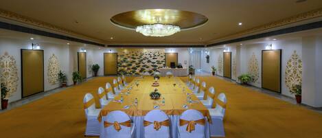 A conference room with a long table, white chairs with gold sashes, a chandelier, and decorative wall panels.