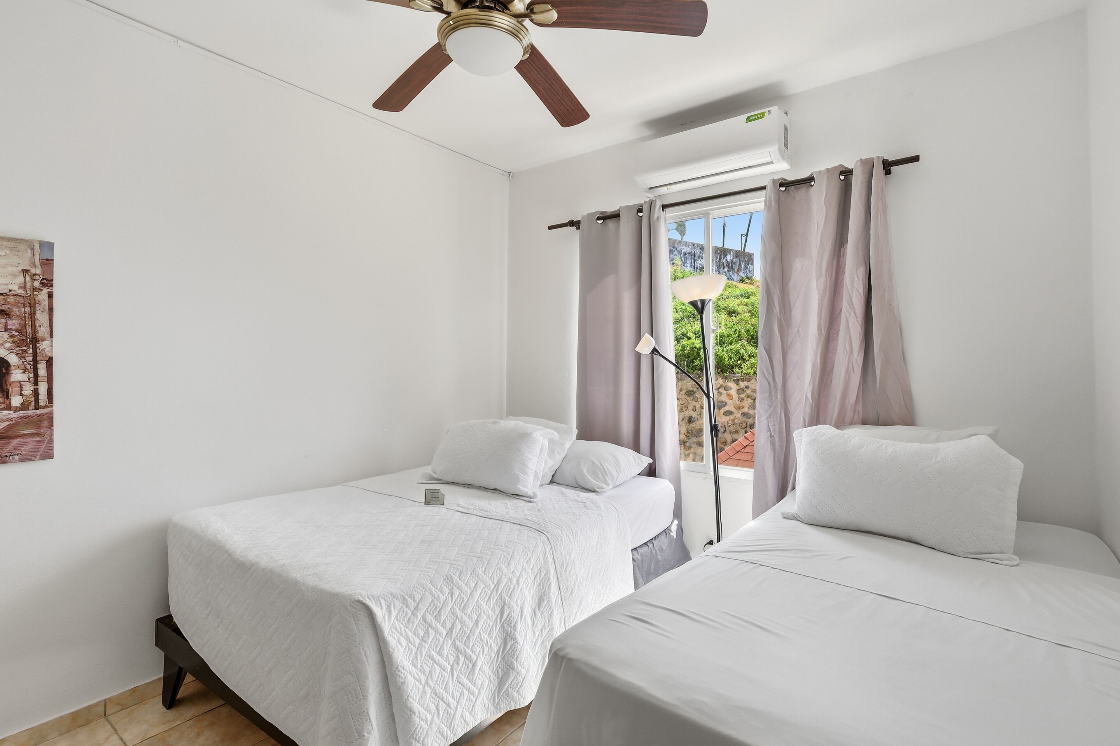 Une chambre avec deux lits, un ventilateur de plafond, un appareil de climatisation et une fenêtre avec des rideaux.