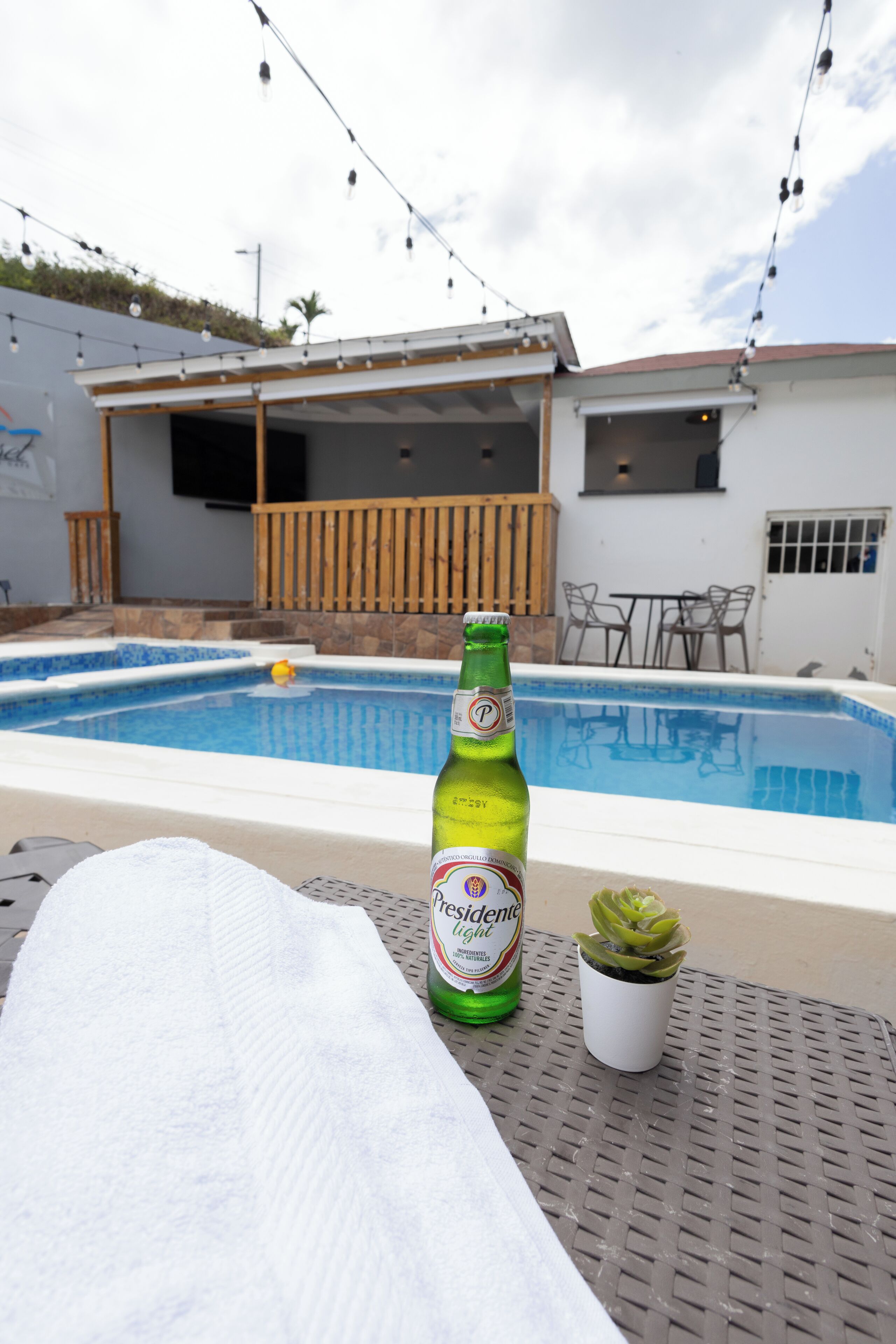 A poolside area with a bottle of beer, a towel, and a small potted plant.