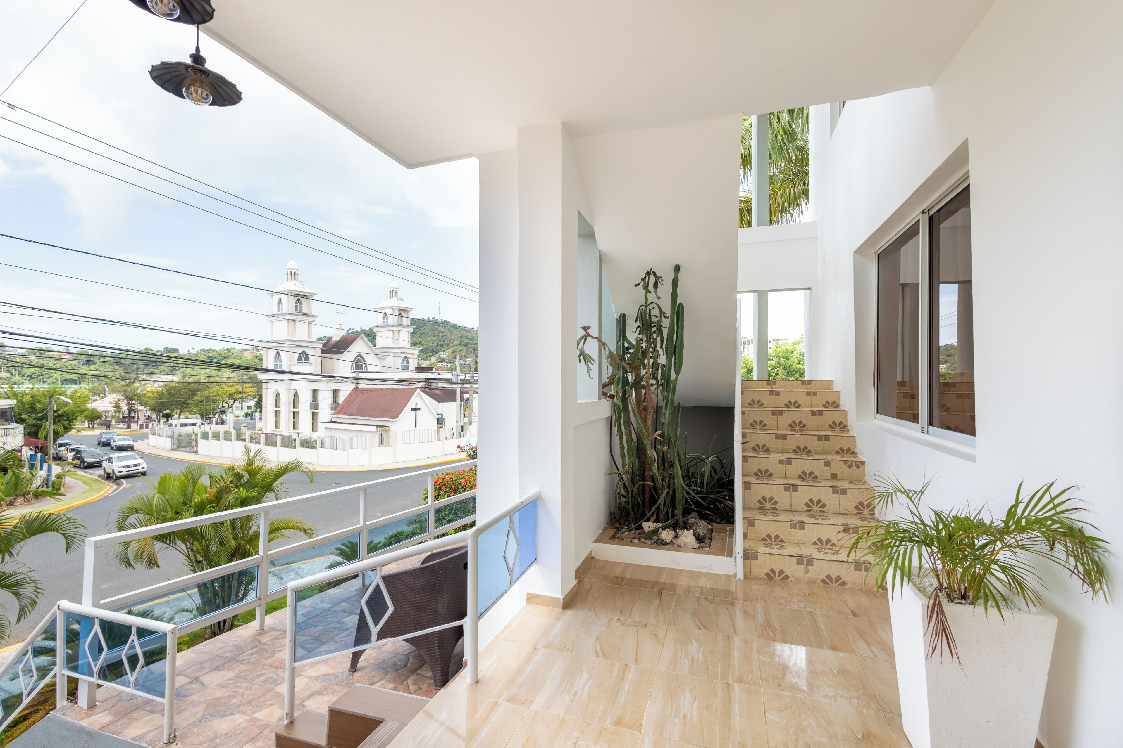 A balcony with a view of a church, a staircase, and a potted plant.