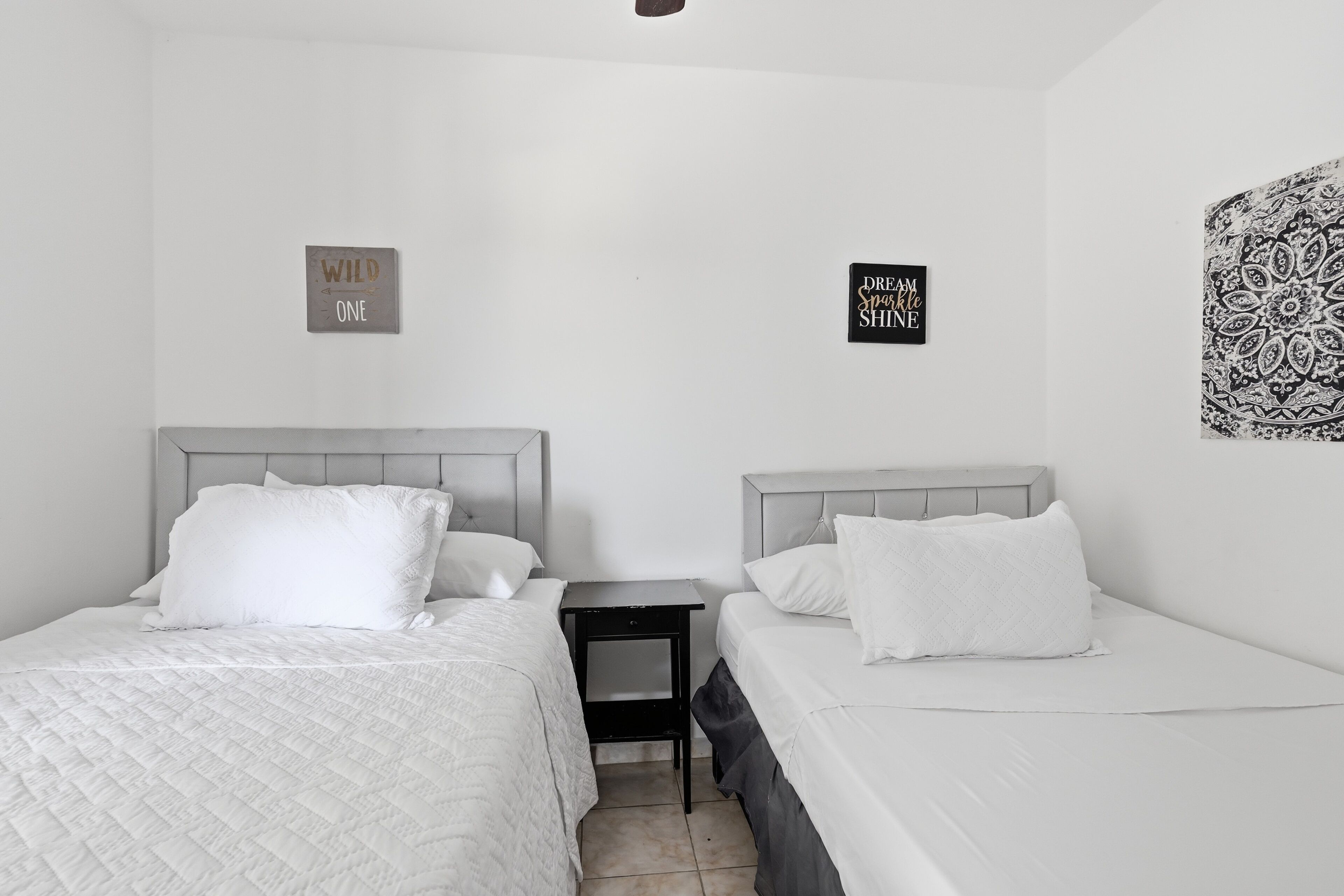 A twin room with two beds, a nightstand, and two wall decorations.