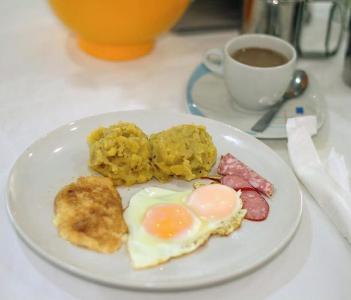Une assiette contenant des œufs brouillés, une galette de pommes de terre, des pommes de terre rissolées et des tranches de saucisse.