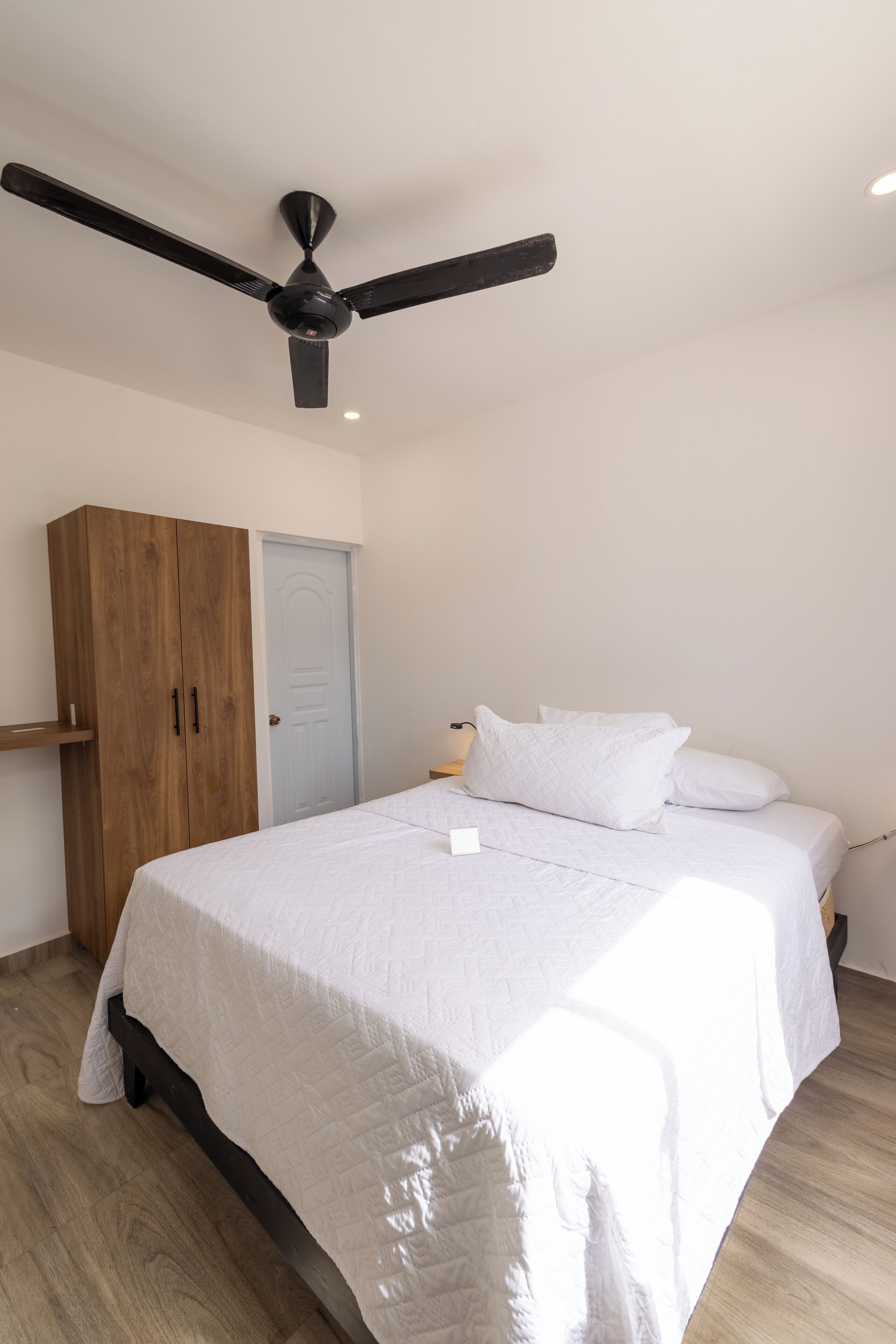 Une chambre à coucher avec un lit, une armoire, une porte et un ventilateur de plafond.