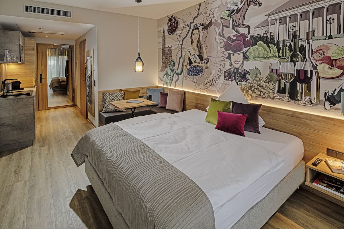Una habitación de hotel moderna con una cama grande, un área de comedor y un mural en la pared.