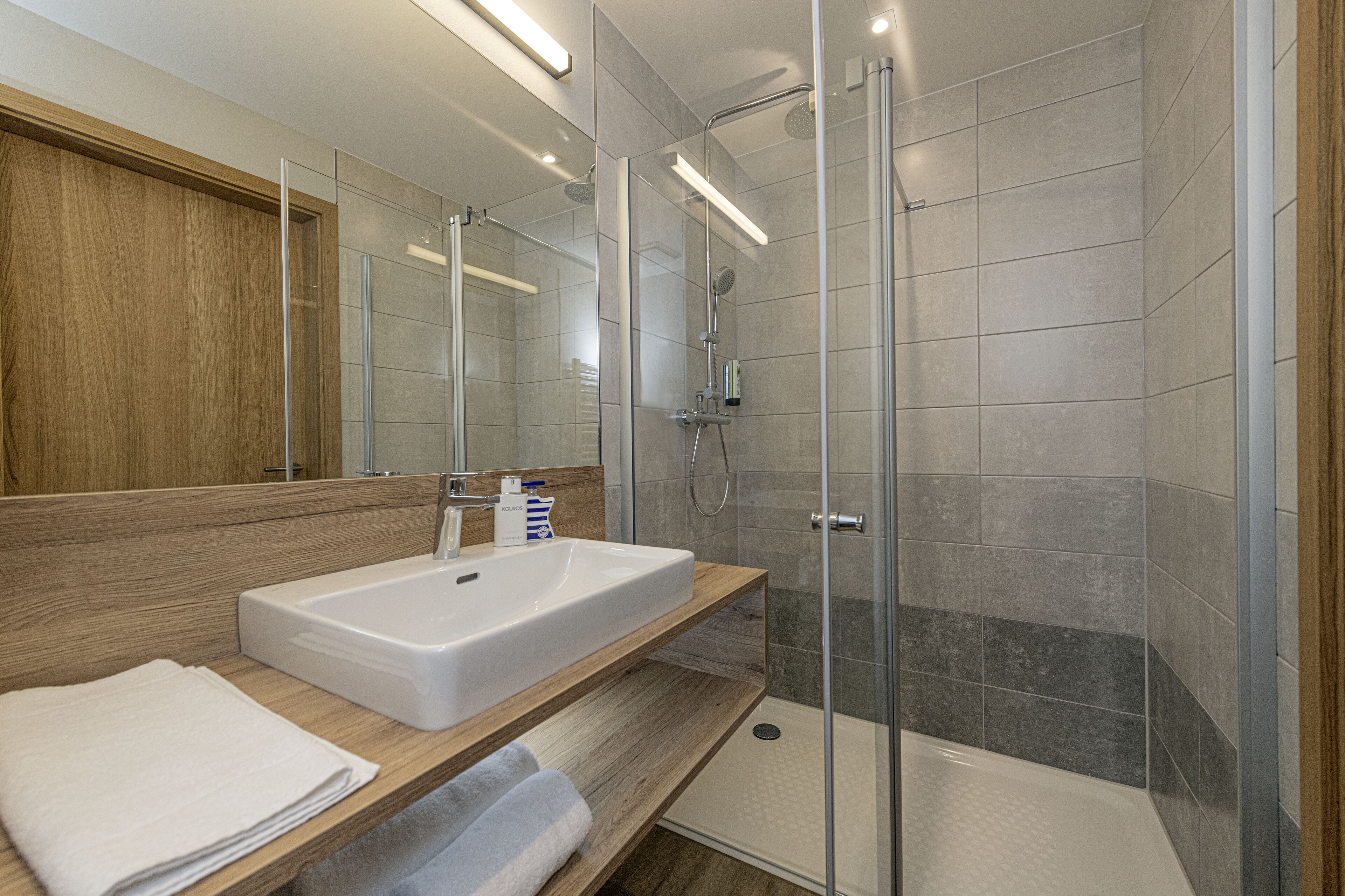 A modern bathroom with a glass-enclosed shower, a wooden vanity, and a large mirror.