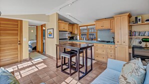 A compact kitchen with wooden cabinets, a central island, and a dining area with a bench. - Stinson Beach Vibe - Easy Living w Garden & Outdoors Shower (Stinson Beach)
