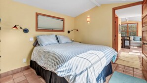 A bedroom with a bed, two wall-mounted lamps, a window with blinds, and a view of a balcony. - Stinson Beach Vibe - Easy Living w Garden & Outdoors Shower (Stinson Beach)