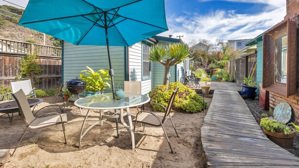 A patio with a table and chairs, a blue umbrella, and a wooden deck. - Stinson Beach Vibe - Easy Living w Garden & Outdoors Shower (Stinson Beach)