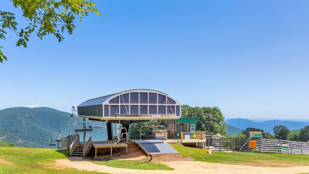 Un edificio moderno con una cúpula de vidrio, un telesilla y un sendero de tierra que conduce a él.
