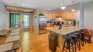 Una cocina moderna con armarios de madera, un refrigerador de acero inoxidable, encimera de granito y una barra con taburetes.