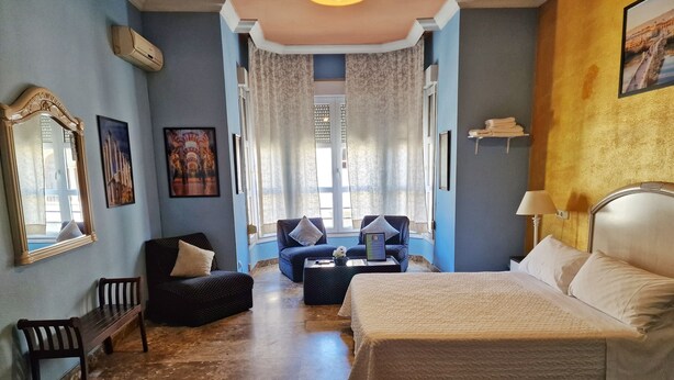 A hotel room with a large bed, two armchairs, a small table, and a window with curtains. - Apartamento El Duque (Córdoba)