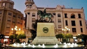 A fountain with a statue in front of a large building with multiple windows and balconies. - Apartamento El Duque (Córdoba)