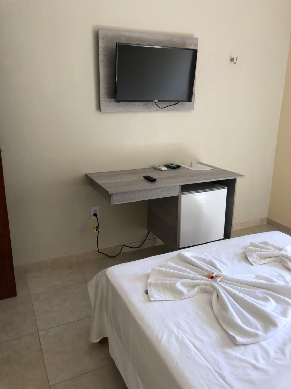 Quarto de hotel com uma cama, uma escrivaninha com televisão de tela plana e um frigorífico pequeno.