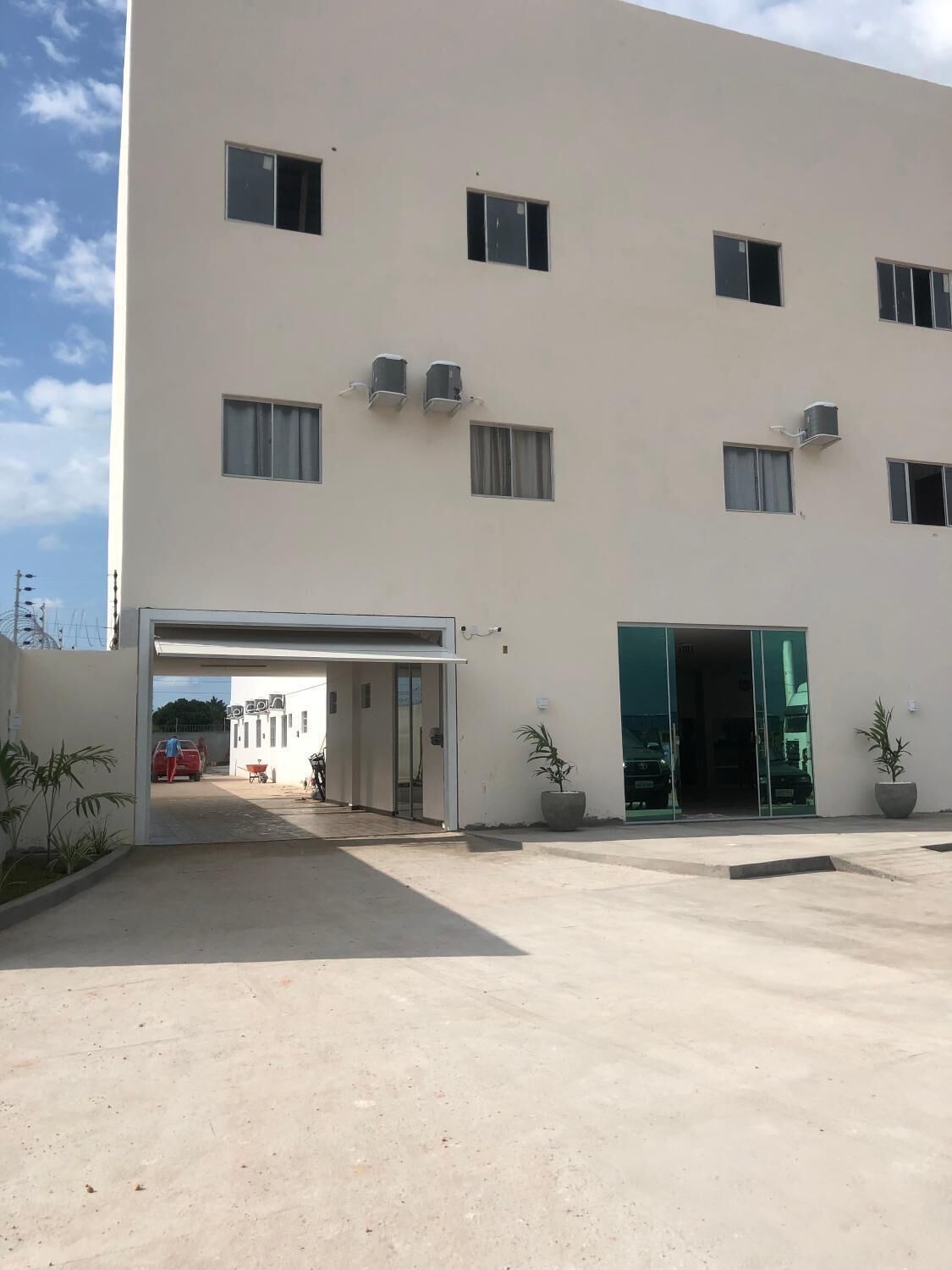 Un edificio moderno con fachada plana, múltiples ventanas y unidades de aire acondicionado. Se observa una entrada cubierta con un coche estacionado en su interior.