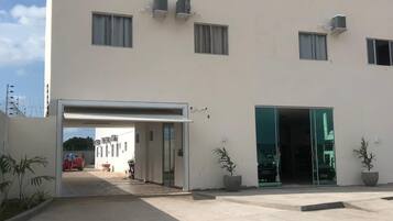 Un edificio moderno con fachada plana, múltiples ventanas y unidades de aire acondicionado. Se observa una entrada cubierta con un coche estacionado en su interior.