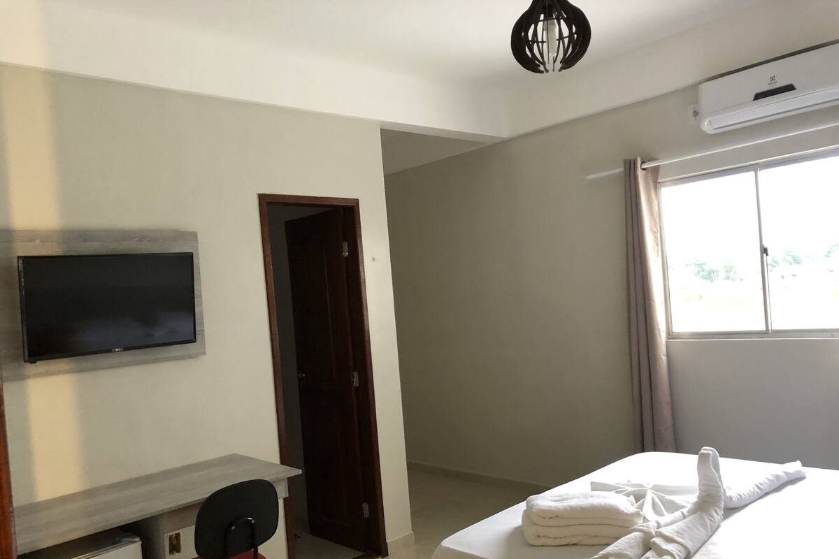 A hotel room with a bed, a desk with a chair, a television, and a window.