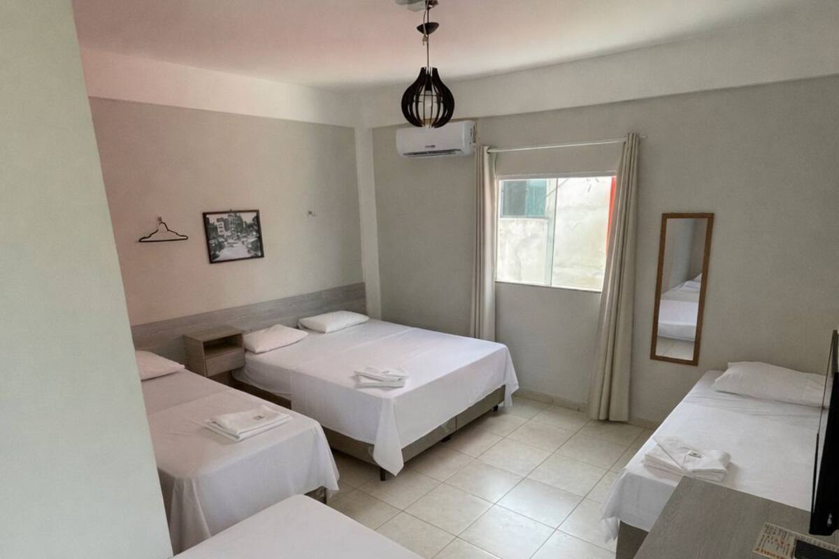 A hotel room with three single beds, a wooden desk, a mirror, and a window with curtains.