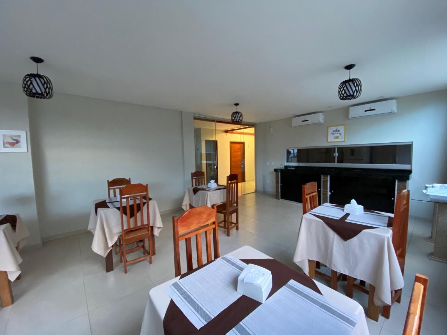 Un comedor con mesas y sillas, una cocina y un equipo de aire acondicionado.