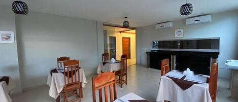 Un comedor con mesas y sillas, una cocina y un equipo de aire acondicionado.