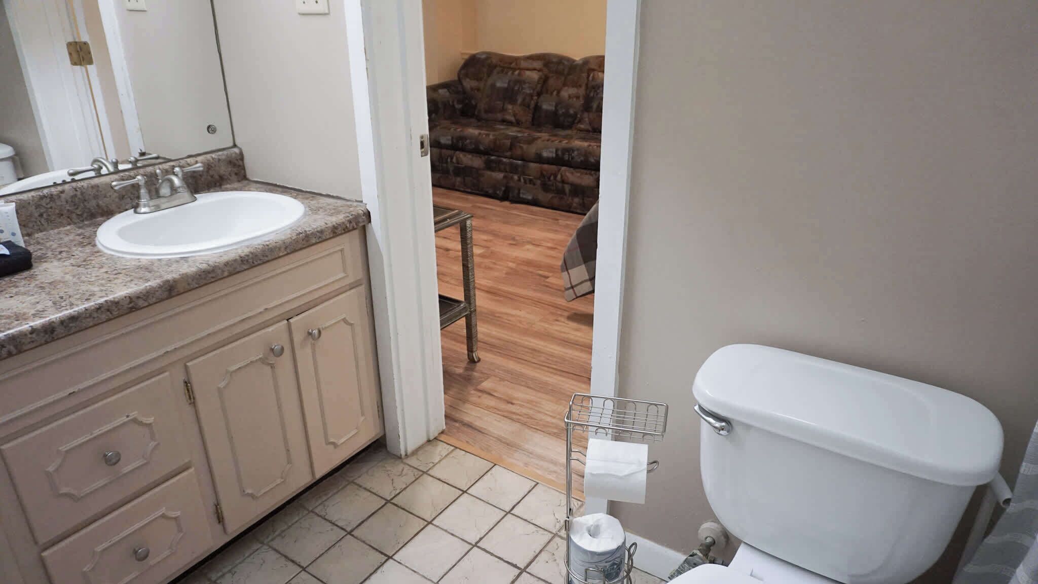 A bathroom with a white sink, beige cabinets, and a toilet.