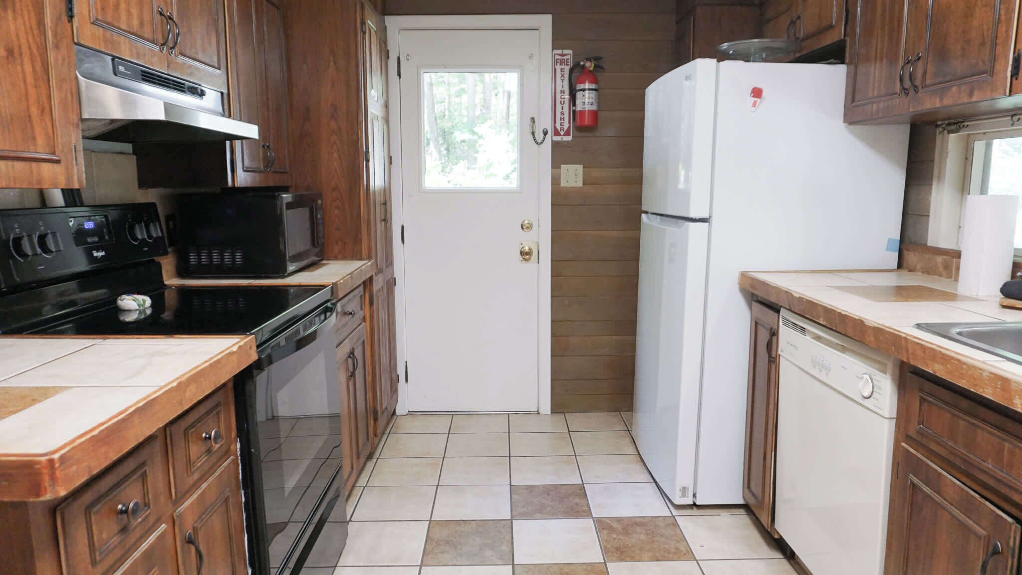 A compact kitchen with wooden cabinets, a white refrigerator, a microwave, an oven, and a dishwasher.