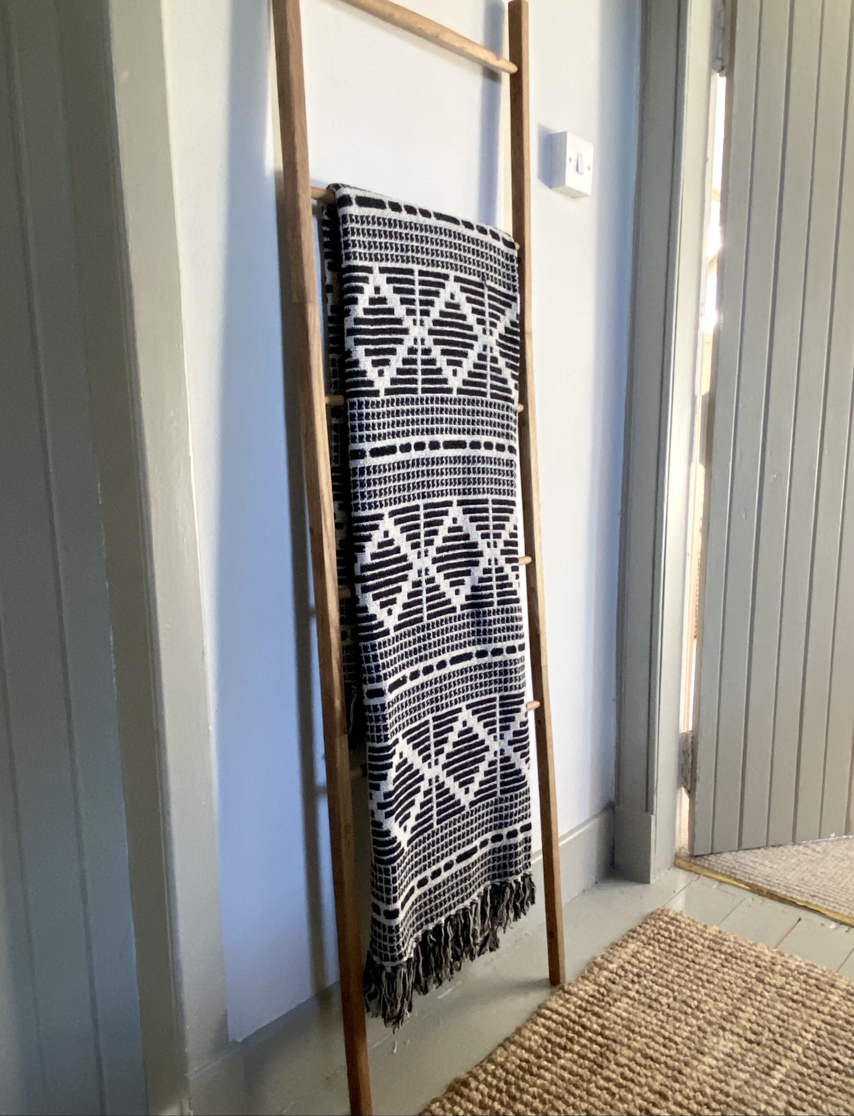A room with a wooden ladder, a patterned blanket, and a woven rug.
