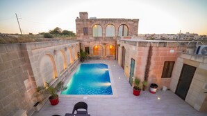 A courtyard with a swimming pool, stone walls, and a building with arched windows.
