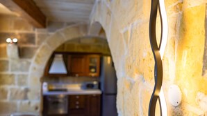 A stone wall with a modern light fixture and a kitchen area in the background.