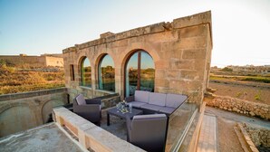 A rooftop terrace with stone walls, a glass-enclosed seating area, and a view of the surrounding landscape.