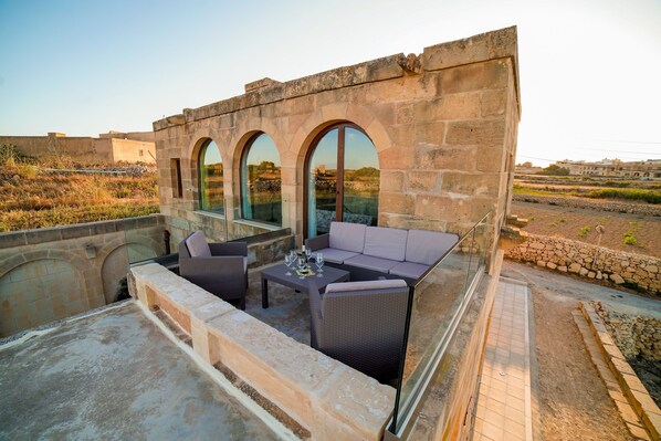 Une terrasse sur le toit, avec des murs en pierre, un espace salon fermé par des baies vitrées et une vue sur le paysage environnant.