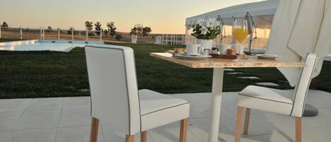 Enjoy an outdoor dining experience with a table set amidst a serene grassy field and a nearby building.