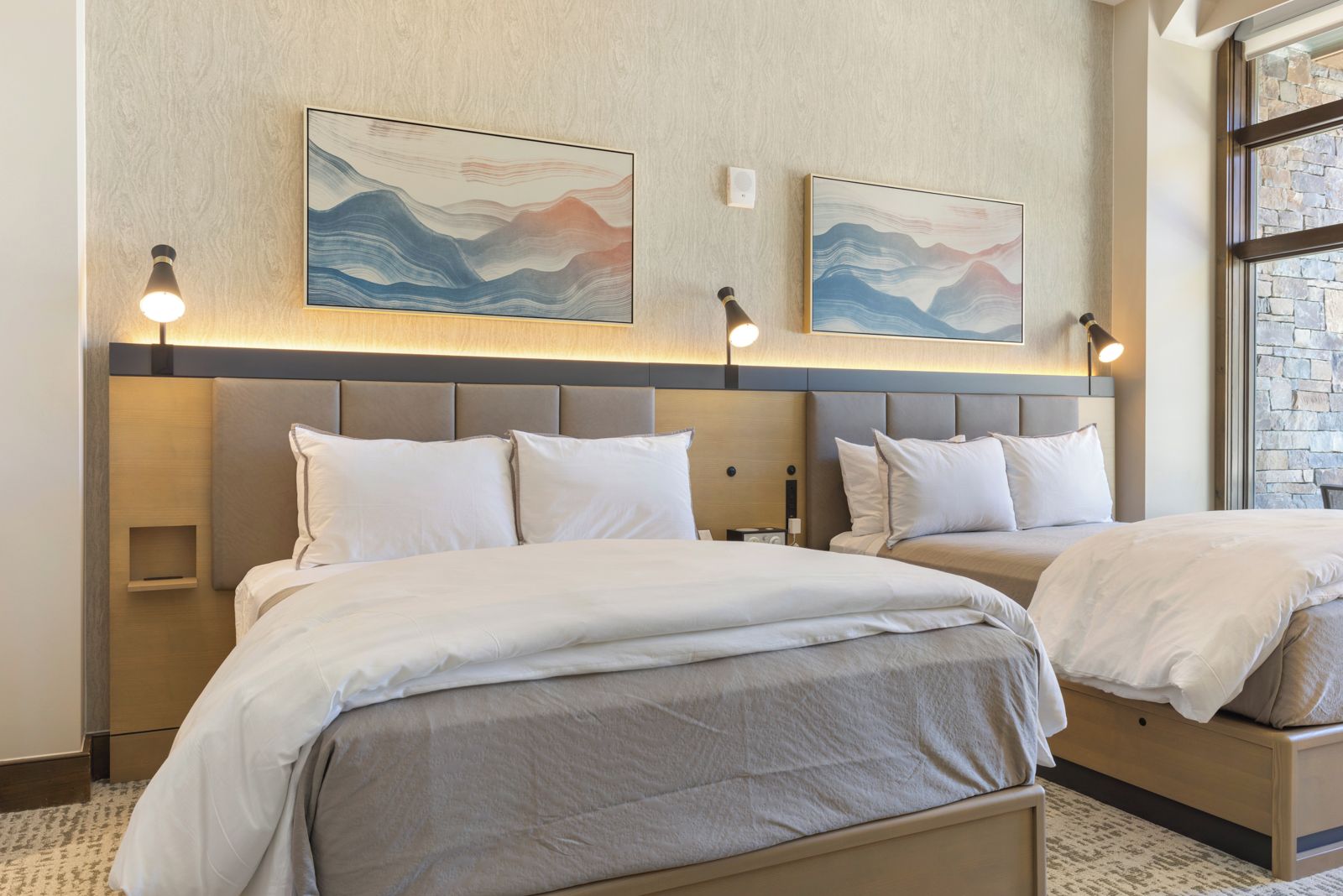 Une chambre d’hôtel avec deux lits, une tête de lit dotée d’un éclairage intégré et des œuvres d’art accrochées au mur.