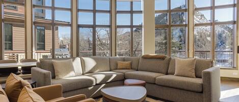 A modern living room with a large sectional sofa, a coffee table, and a view of a snowy mountain landscape through large windows.