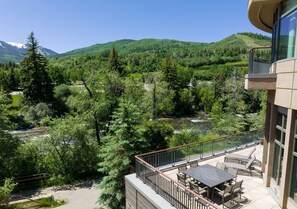 A balcony with outdoor furniture overlooking a river and forested hills. - Charlie's Slopeside: Remodeled, Sleeps 12, Huge Wraparound Deck, Gondola, Views + Resort Amenities (Avon)