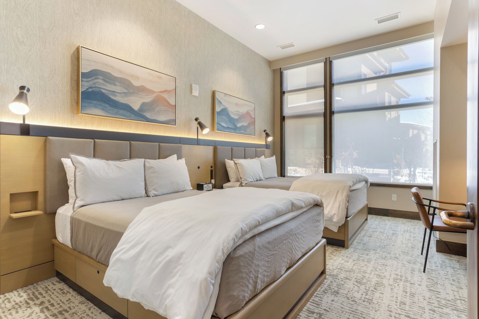 Une chambre d’hôtel moderne avec deux lits, une grande fenêtre et des œuvres d’art accrochées au mur.